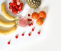 A vibrant flat lay of tropical fruits including bananas, strawberries, and a smoothie on a white background.